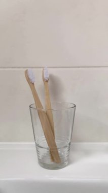 Bir kadının eli bambu çocuk diş fırçasını yetişkin diş fırçasıyla dolu bir bardağa koyar. 4K dikey video. Banyo da biyolojik çözünebilir hijyen ürünleri var..