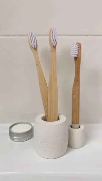 コンクリートスタンドの子供と大人の竹の歯ブラシ 歯磨き粉について 垂直ビデオ バスルーム内の生分解性衛生製品 — ストック動画