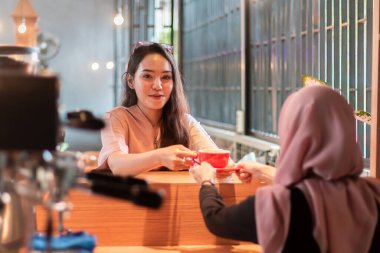 Kahve dükkanında sipariş bekleyen müşterilere bir fincan kahve veren güzel bir Asyalı barista.
