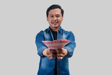 Elinde kağıt para tutarken ve kameraya bakarken mutlu bir yüz ifadesi gösteren genç Asyalı adam.