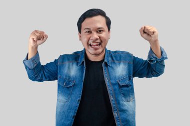 Genç Asyalı adam, kutlama jesti olarak yüzünde mutlu bir gülümsemeyle yumruğunu kaldırdı. İzole edilmiş arkaplanda