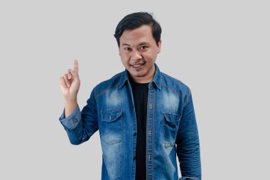 Asyalı genç adam izole edilmiş arka planda elini boş bir alana doğrultuyor.