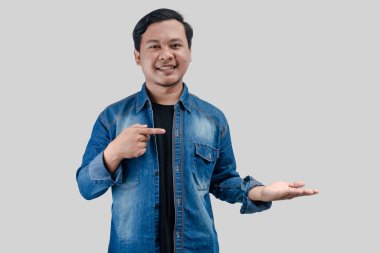 Genç Asyalı adam parmak işareti ile kenara çekilerek izole arka plandaki fotokopi alanı reklam ürününe el hareketi yaptı