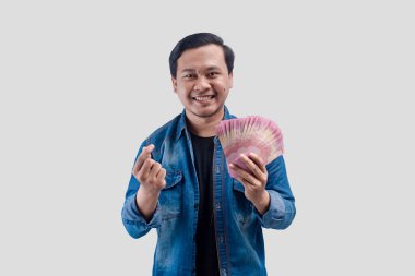 Kağıt para ve aşk işareti tutan Asyalı genç adam gülümseyen yüz ifadesi sergiliyor.