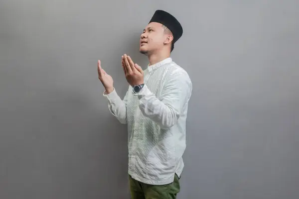 stock image Asian Muslim man wearing a koko shirt and peci with shades of the fasting month, standing looking empty space happily to show grateful , isolated on a gray background