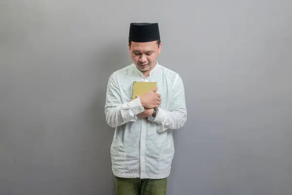 亚洲穆斯林男子 身穿可可可豆衬衫 头戴山核桃色的禁食月 手持祈祷珠子 古兰经 与灰色背景隔离 — 图库照片