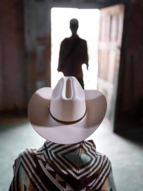 Tanımlanamayan genç bir Meksikalı şapkası ve pançosu olan gizemli bir siluetin önünde bekliyor. Batı dövüş sahnesi kavramı