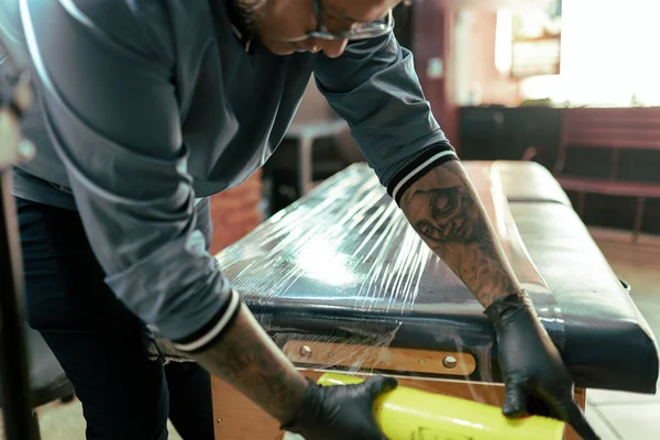 A tattoo artist is covering his studio stretcher with plastic film. Concept of hygiene in the tattoo studio