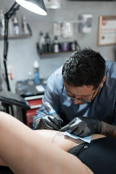 A tattoo artist is tattooing a snake on a womans leg. Concept of tattoo studio