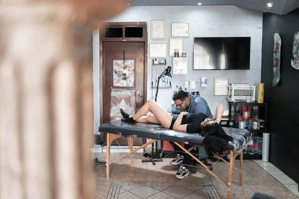 A tattoo artist is tattooing a snake on a womans leg in his work studio. Concept of tattoo studio