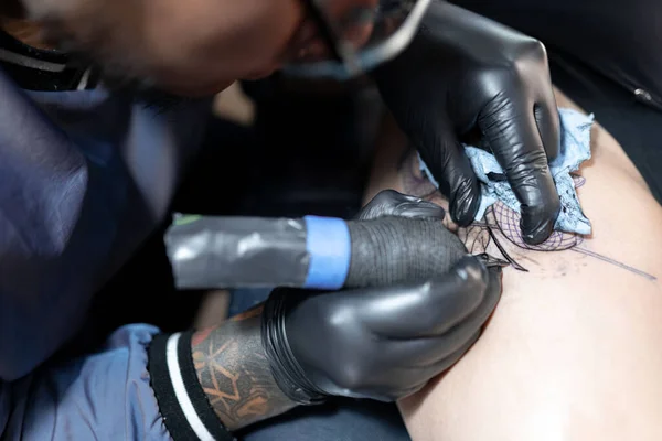 A tattoo artist is tattooing a snake on a womans leg. Close up. Concept of tattoo studio
