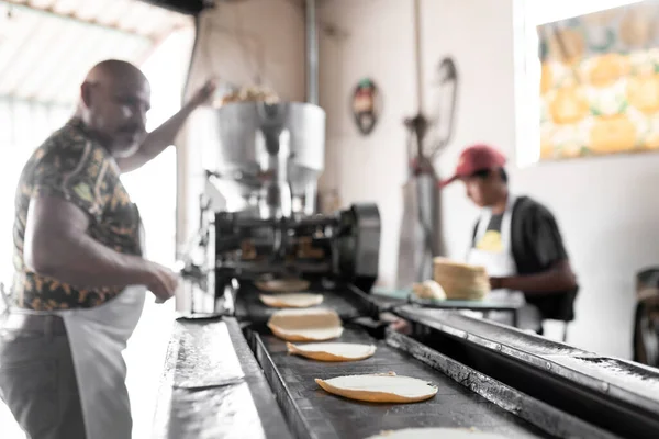 An adult man is working with his son producing corn tortillas with a nixtamall mill. Concept of traditional corn tortillas preparation