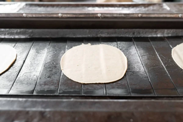 A gas stove conveyor belt is carrying some corn tortillas. Concept of traditional corn tortillas preparation