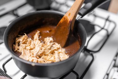 A young woman is mixing chicken with mole sauce using a gas stove. Concept of mexican picnic day