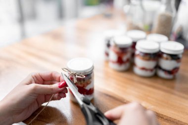 A young woman is cutting a decorative bow of a jar filled with yogurt, fruits and cereal. Concept of mexican picnic day