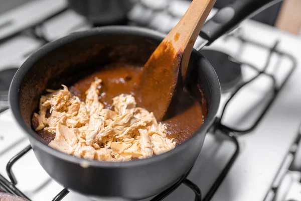 A young woman is mixing chicken with mole sauce using a gas stove. Concept of mexican picnic day