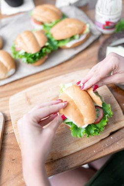 A young woman is closing a healthy sandwich with lettuce, avocado and tomato at home. Concept of mexican picnic day