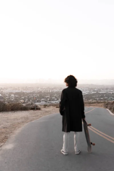 A view of Los Angeles cityscape with a blurred young man looking holding his skate in Baldwin Hills during the sunset, Los Angeles. Concept of skate lifestyle