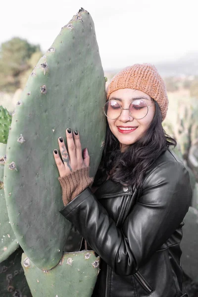 Portrait of a young woman hugging a big nopal tuna in a field during the sunrise. Concept of mexican fashion