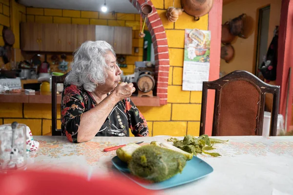 A senior mexican woman is eating a fresh cooked chayote for a snack on a table in the dining room. Concept of mexican traditional cooking