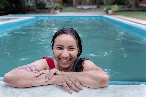 Yüzme havuzunun kenarında kırmızı mayo giymiş genç bir İspanyol kadının portresi.