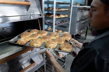 Genç bir İspanyol fırıncı fırından taze pişmiş tatlı ekmeklerle dolu bir tepsi çekiyor. Geleneksel Meksika tatlı ekmek sanatı kavramı