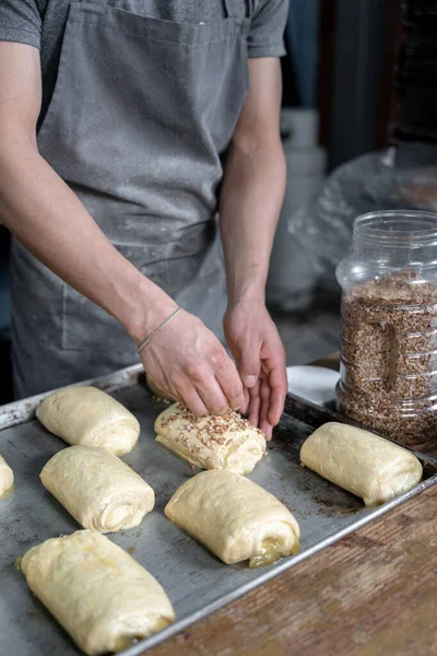 Genç bir İspanyol adam, gri üniformalı bir tepside pişirmeden önce tatlı fındıklı çörekleri kremayla kaplıyor. Geleneksel Meksika tatlı ekmek sanatı kavramı
