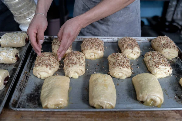 Genç bir İspanyol adam, gri üniformalı bir tepside pişirmeden önce tatlı fındıklı çörekleri kremayla kaplıyor. Geleneksel Meksika tatlı ekmek sanatı kavramı