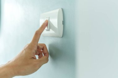 Closeup of finger is turning off on lighting switch on blue wall at home. Power, Energy, Saving Electrical, Copy space.