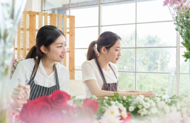 Asian Korean female florists working on laptop in flower store, chatting with clients, Small business, taking customer order, Entrepreneur