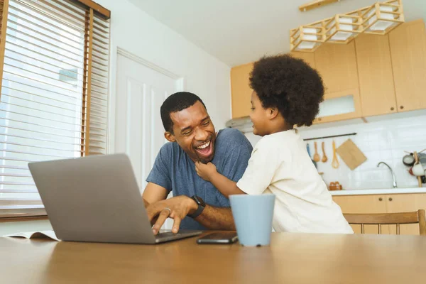 美国黑人父亲在家里用笔记本电脑干活 而他快乐的儿子在厨房里让他分心 — 图库照片