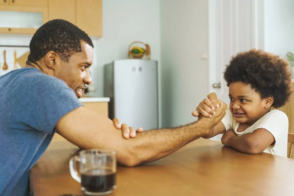 美国黑人父亲在家里的厨房里和他的小男孩扭臂比赛 — 图库照片