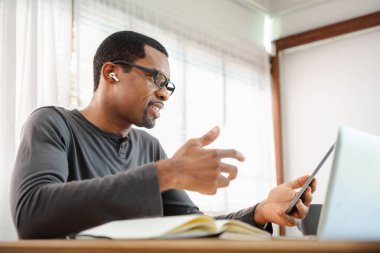 Siyah Afrikalı Amerikalı adam dijital tabletten video görüşmesi yapıyor. Afrikalı erkek Freelancer iş arkadaşı, iş arkadaşı ya da takımla laptopta çalışıyor, evde çalışıyor.