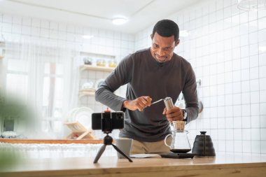Siyah Afro-Amerikan erkek mutfakta kahve damlatıyor, sıcak içecek evde kahve içiyor, cep telefonuyla video görüşmesi yapıyor..