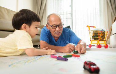 Mutlu Asyalı kıdemli Japon adam ve küçük çocuk yerde birlikte oynuyorlar. Dedem ve torunum renkli pastel boyalarla resim yapmayı seviyorlar..