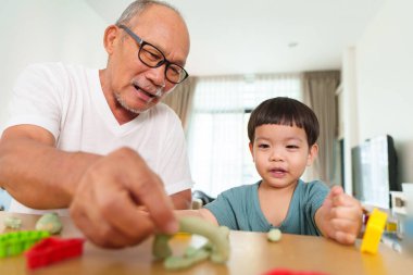 Gülümseyen Asyalı son sınıf öğrencisinin portresi ve küçük çocuk killeri birlikte şekillendiriyor. Büyükbabam ve torunum plastikten oyuncak yapıyorlar. Yaratıcılık ve hobi.