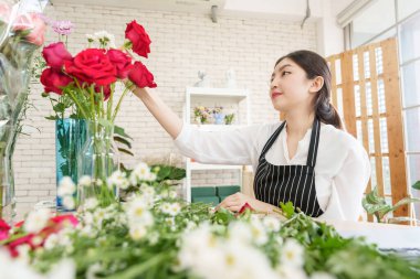 Güzel Asyalı kadın çiçekçi çiçekçide güzel kırmızı güller yapıyor, küçük işletme sahibi, girişimci