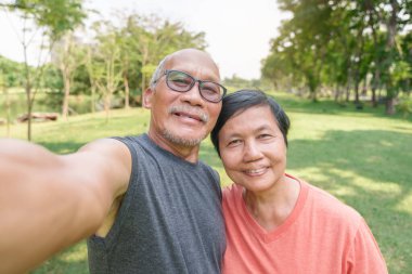 Mutlu gülümseyen Asya kıdemli Çinli çiftin portresi parkta egzersiz yaparken akıllı telefonla selfie çekiyorlar. Açık havada cep telefonu kullanan yetişkinler.