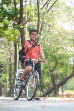 Kasklı, cep telefonu ya da akıllı telefon taşıyan ve dışarıda bisikletle seyahat ederken selfie çeken mutlu Asyalı kıdemli Çinli adam. Emeklilik aktivitesi, Rahatlama, Egzersiz, Sağlık ve yaşam tarzı