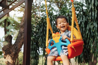 Parkta salıncakta sallanırken gülen küçük Asyalı çocuk..
