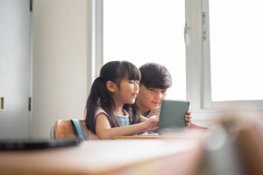 Mutlu Gülümseyen Asyalı iki ilkokul öğrencisi okulda dijital tablet bilgisayar kullanıyor..