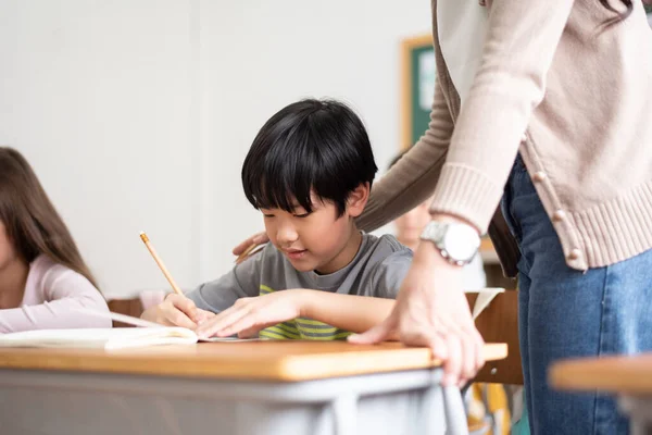 Азиатский Мальчик Японец Пишет Столом Классе Учительница Помогает Детям Столом — стоковое фото