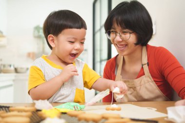 Asyalı anne ve küçük oğlu kremayla zencefilli kurabiye yapıp süslüyorlar. Kurabiye, yemek hazırlama, yemek pişirme..