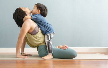 Evde yoga meditasyon yaparken annesine sarılan Asyalı çocuk. Küçük oğluyla yoga minderinde oynayan bir kadın..
