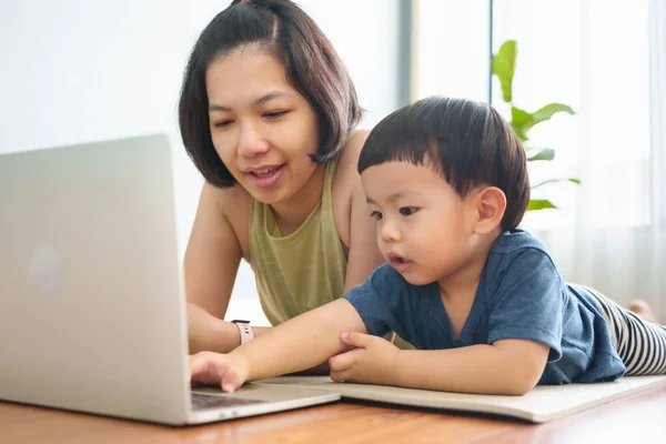 Asian chinese mother and little son using Laptop while practicing yoga exercise on the floor. Woman teaching adorable boy using computer.