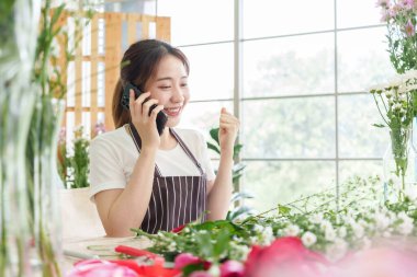 Neşeli Güzel Koreli Kadın akıllı telefondan iyi haberler alıyor. Asyalı çiçekçi kadın müşterilerden emir alırken kutlama yapıyor.
