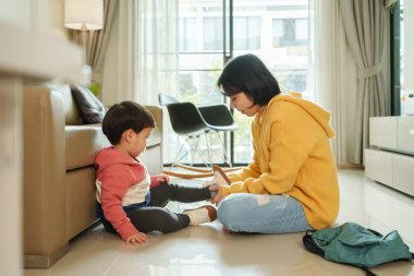 Asyalı bir anne oğlunun ayakkabılarını giymesine yardım ediyor.