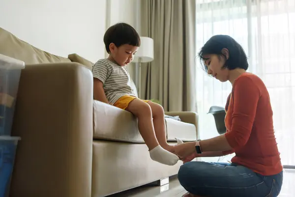 Asiática China Madre Poniendo Calcetines Pequeño Hijo Pies Sofá Casa Imagen De Stock