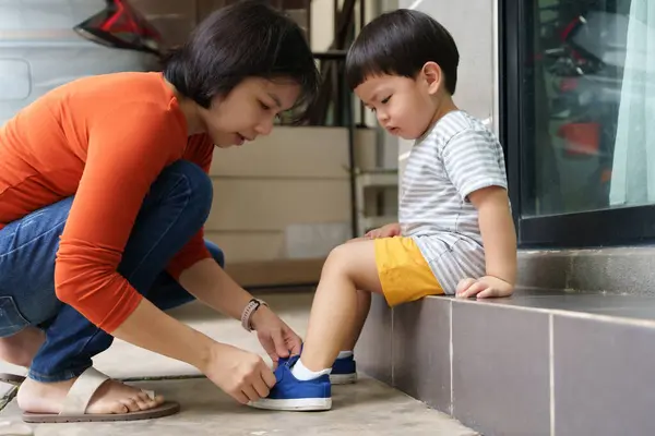 Asyalı Çinli Anne Oğlunun Dışarıda Ayakkabılarını Giymesine Yardım Ediyor Okulun - Stok İmaj