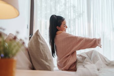 İçerik Asyalı Kadın Uyanıyor, Güneşli bir yatak odasında kollarını rahatlıkla uzatıyor, Dinginliği Yaşıyor